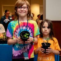 two elementary students holding newly potted seedlings at student project showcase
